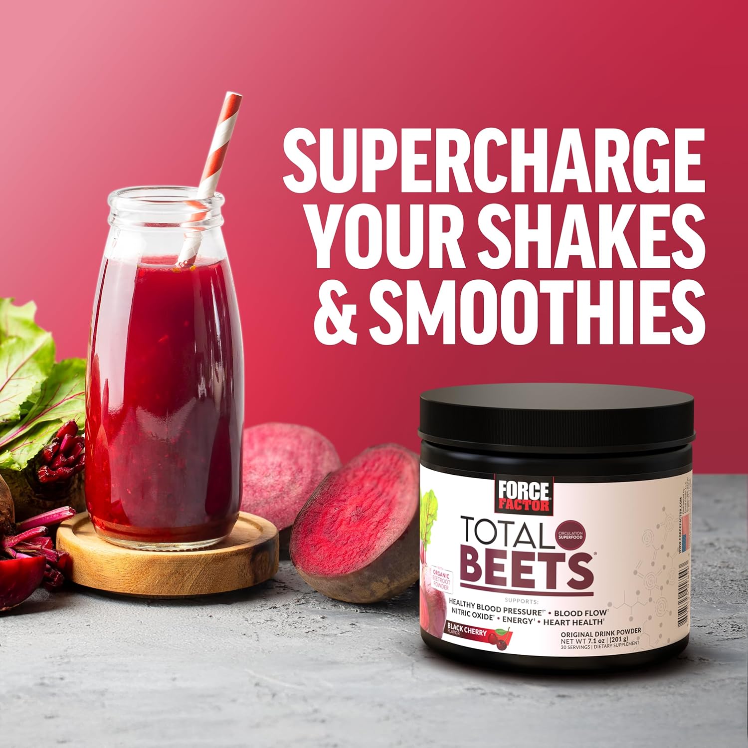Glass of red shake with a straw, jar of Total Beets powder, and beets on a gray surface with red background.