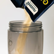 Chocolate protein powder being poured from a sachet into a shaker bottle.